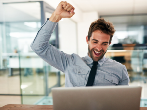 Happy man cheering at laptop.